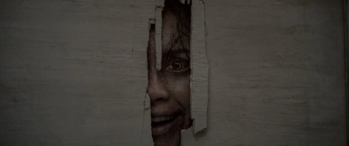 Mulher espia por um buraco na parede em cena de A Morte do Dem&ocirc;nio: Em Chamas, terror dispon&iacute;vel na HBO Max