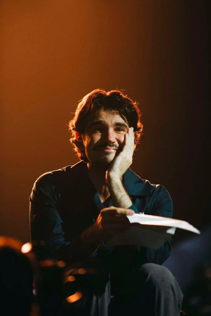 Jão sorrindo sentado no palco durante a gravação com fãs no Spotify
